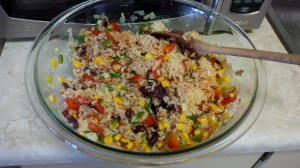A glass bowl filled with kidney beans, rice, corn, and tomatoes all stirred with a wooden spoon