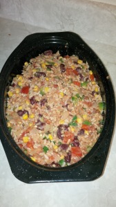 A casserole dish filled with filling, comprising rice, kidney beans, corn, green onions, and tomatoes
