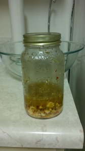A mason jar filled 1/4 of the way. At the bottom are chunks of feta, covered in oil, dried rosemary, and red chili pepper flakes